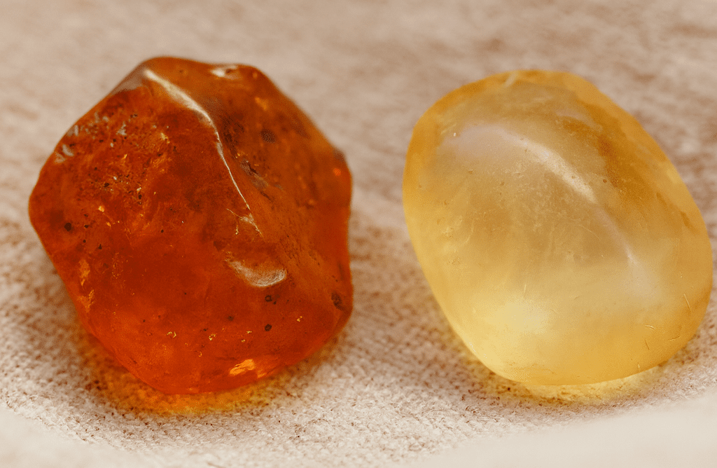Raw amber and copal resin stones displayed on linen fabric, showing color and texture differences for jewelry identification