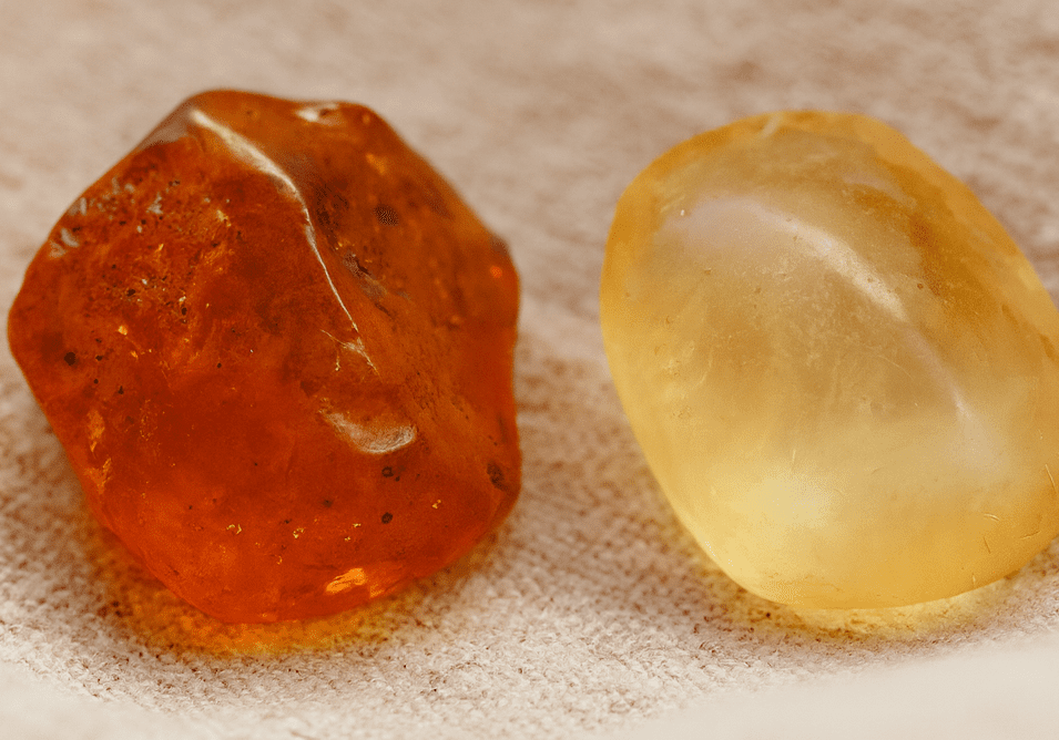 Raw amber and copal resin stones displayed on linen fabric, showing color and texture differences for jewelry identification